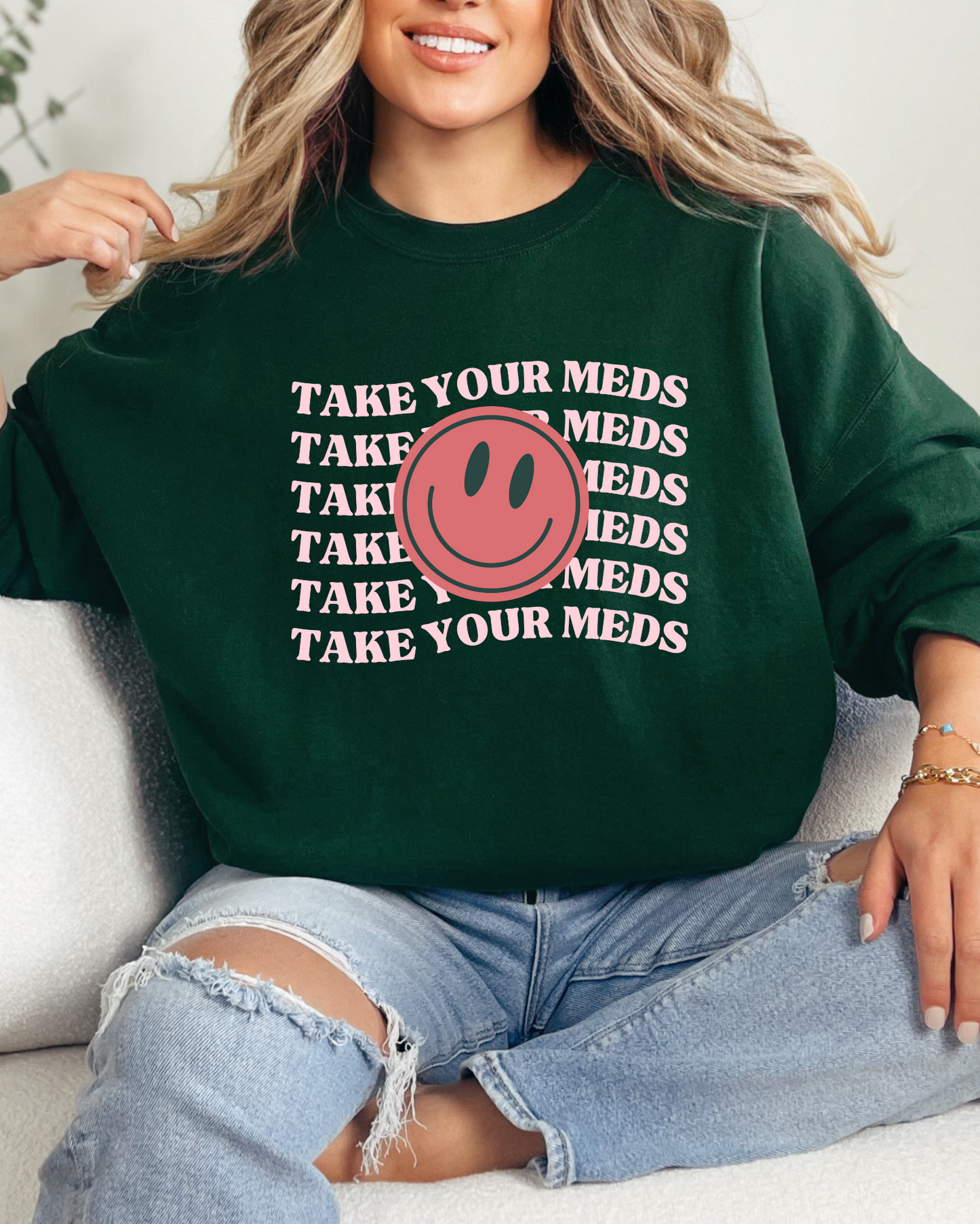 Person wearing a green sweatshirt with a smiley face and text, sitting on a couch.