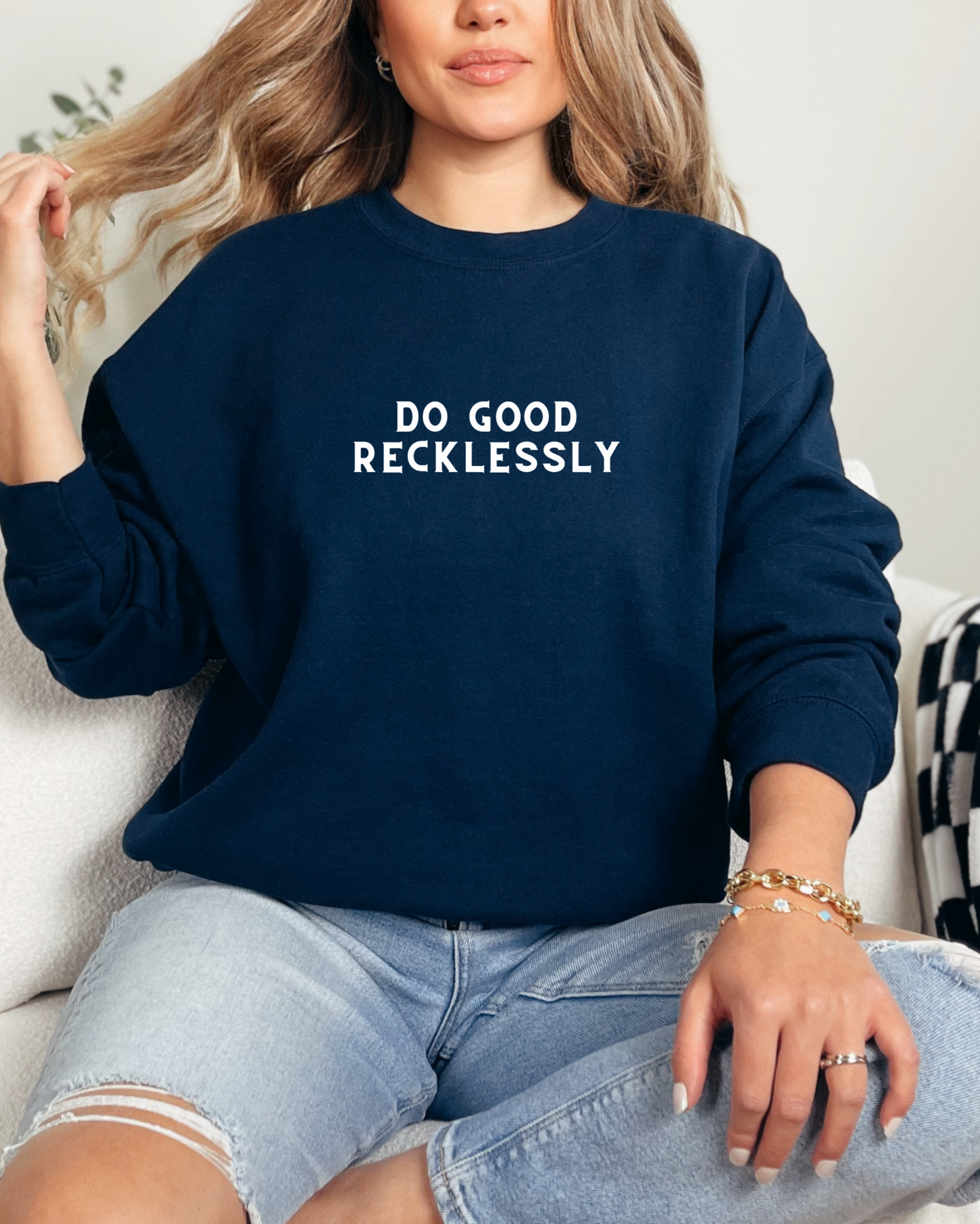 Person wearing a navy blue sweatshirt with 'DO GOOD RECKLESSLY' text, sitting on a white couch.