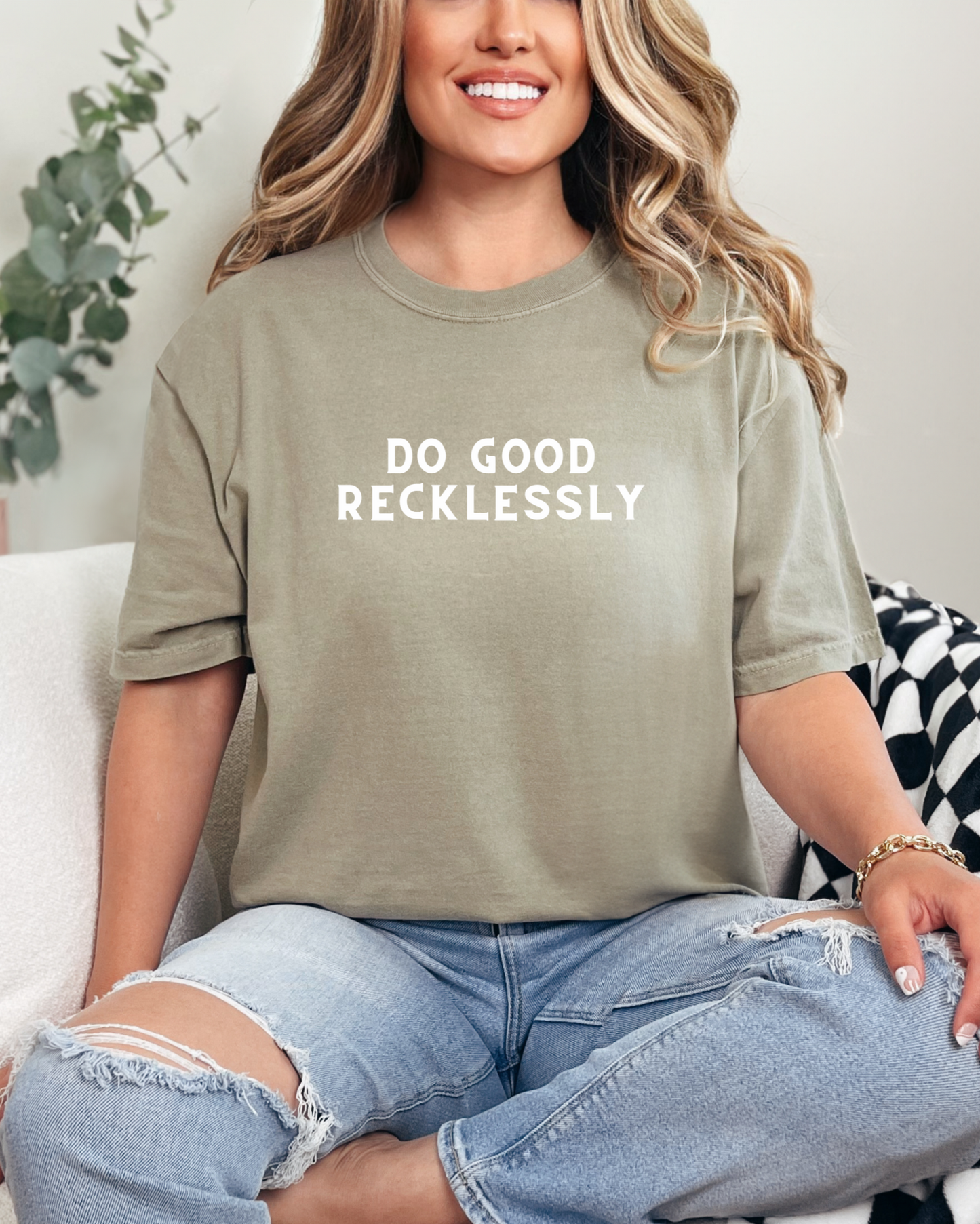 Woman wearing a t-shirt with 'DO GOOD RECKLESSLY' text, sitting on a couch.