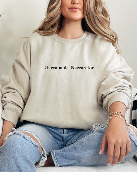 Person wearing a beige sweatshirt with 'Unreliable Narrator' text, sitting on a couch.