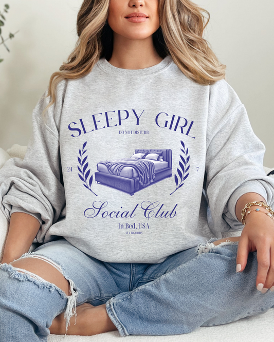 Person wearing a 'Sleepy Girl Social Club' sweatshirt sitting on a couch.