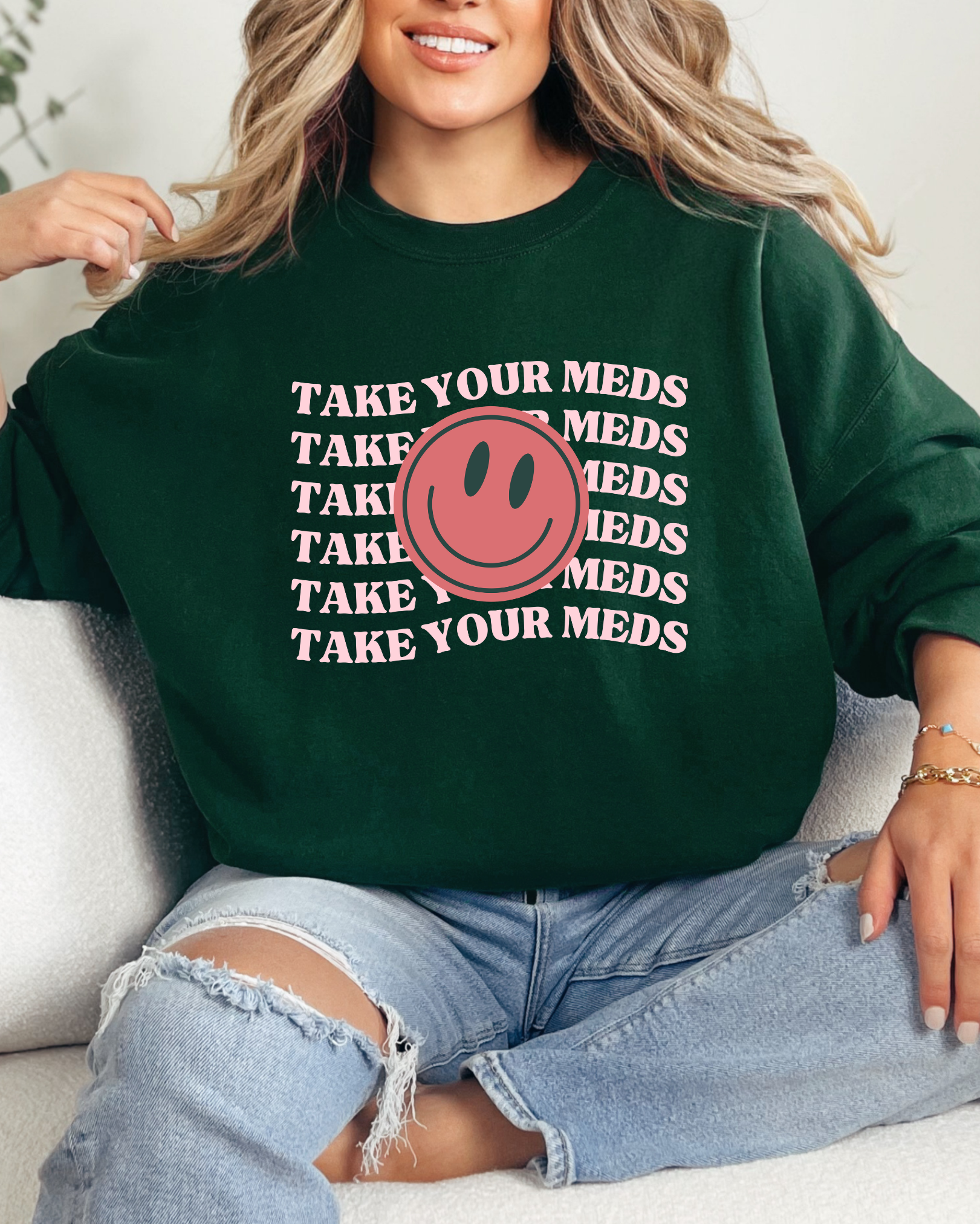 Person wearing a green sweatshirt with a smiley face and text, sitting on a couch.