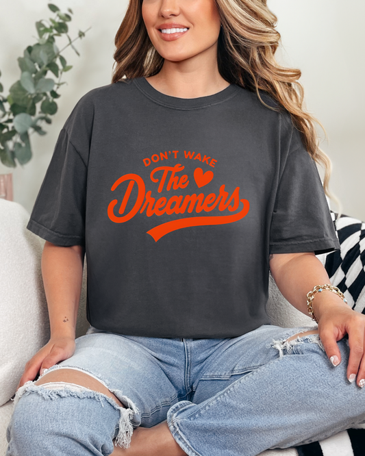 Woman wearing a dark gray t-shirt with orange text sitting on a couch.