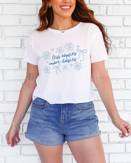 Woman wearing a white t-shirt with blue floral designs and text against a white brick wall.
