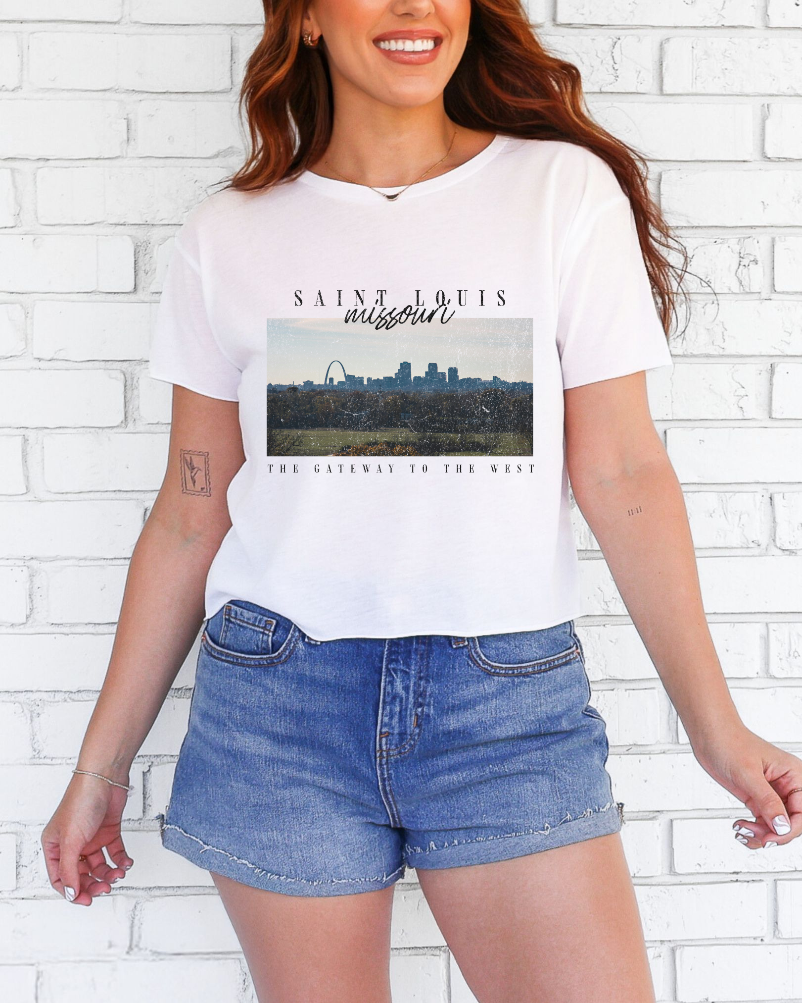 Person wearing a white t-shirt with a graphic design in front of a white brick wall