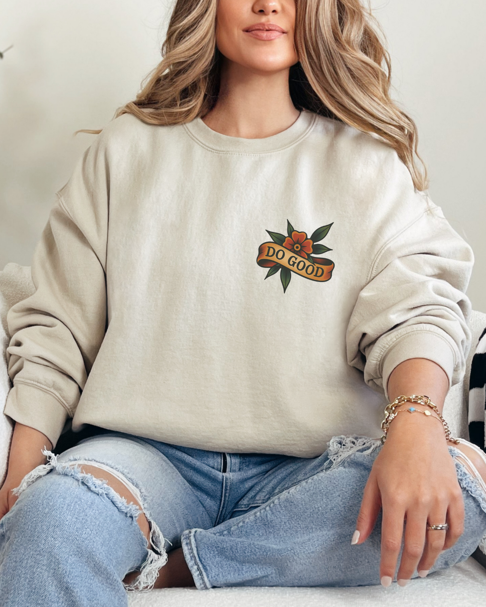 Woman wearing a beige sweatshirt with a logo sitting on a couch.